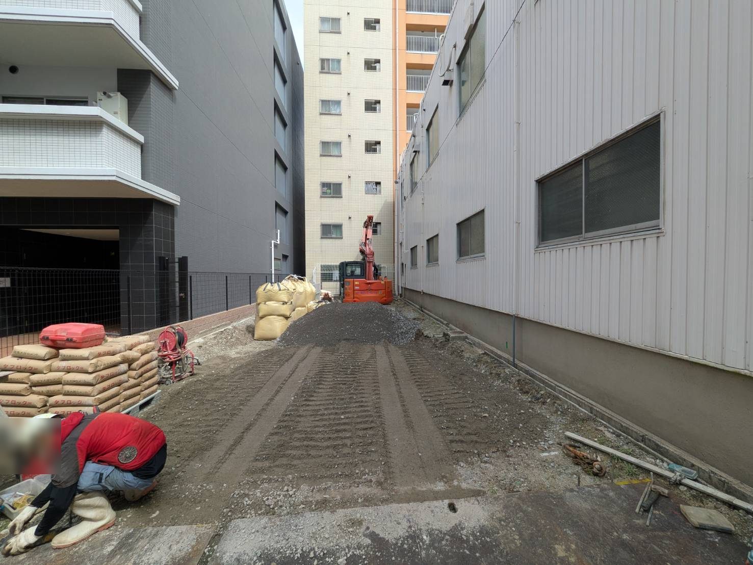 セメント系固化材(袋)を搬入し、小型バックホウで土と混合。間口の狭い敷地に合わせた機械の選定です。